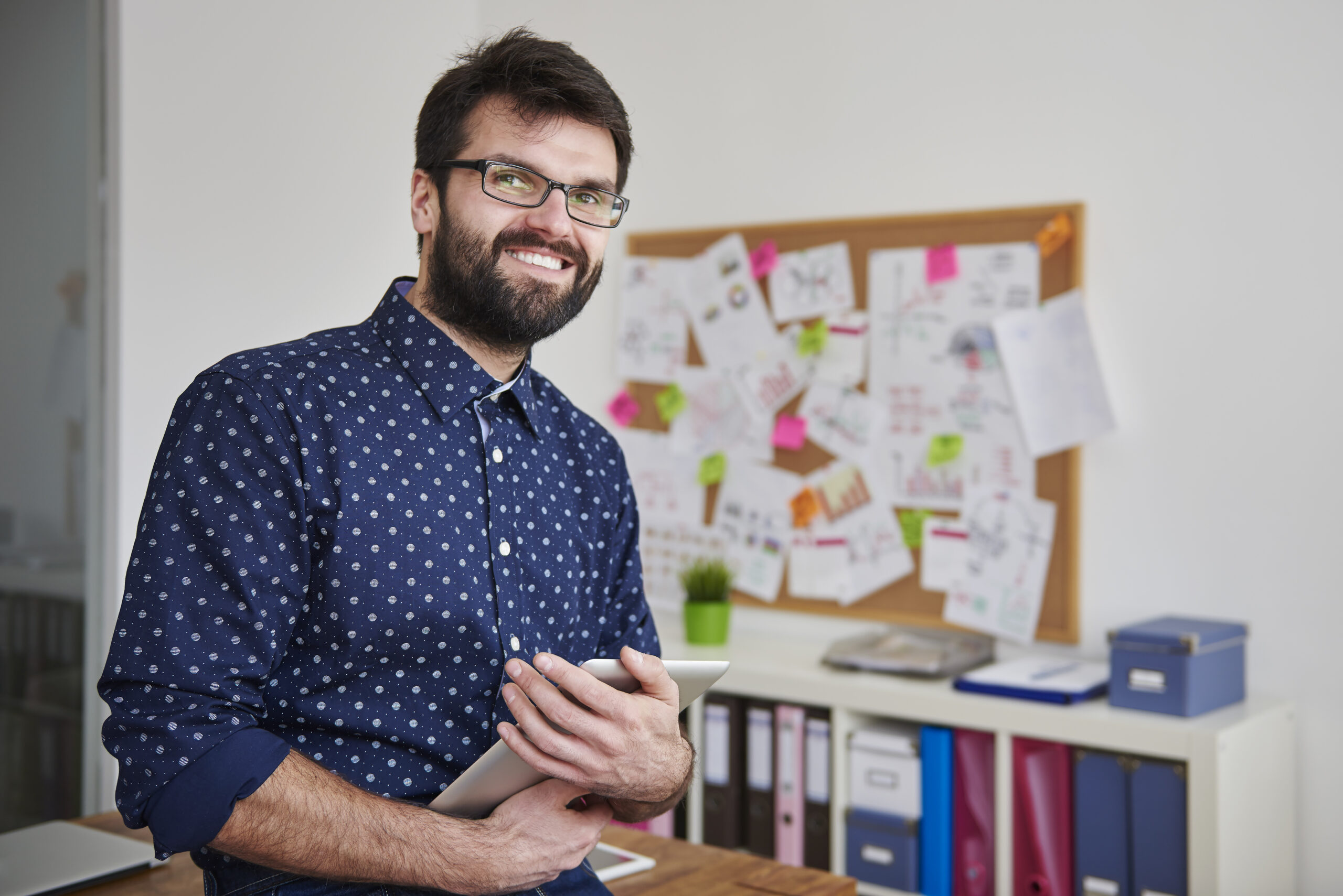 Happy man stood in front of notice board clearly supporting or directing business people